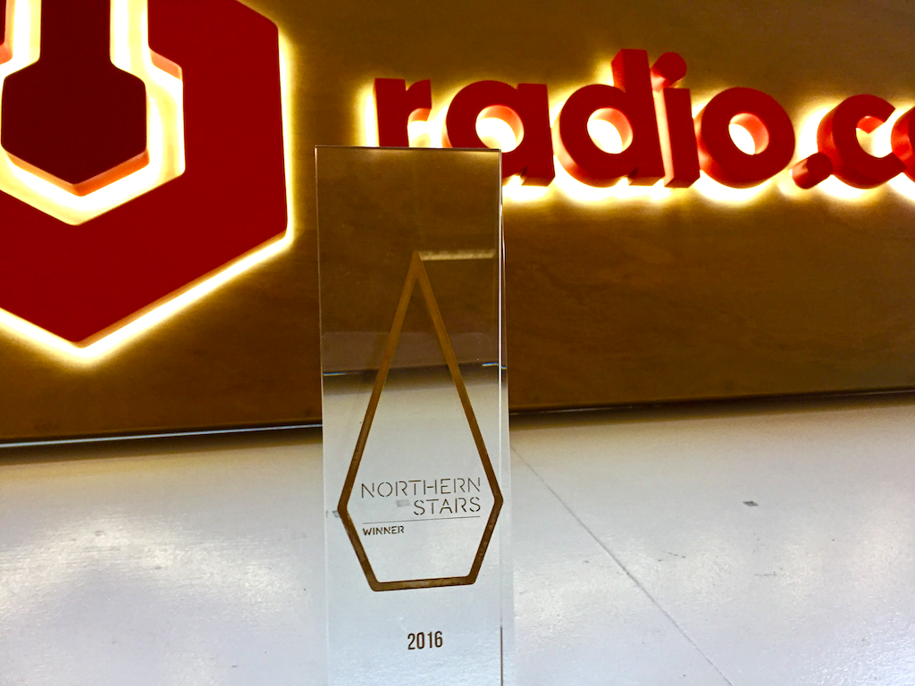 This is an image of a glass Northern Stars Award in front of a brown and red backdrop, the Radio.co logo in warm lights.