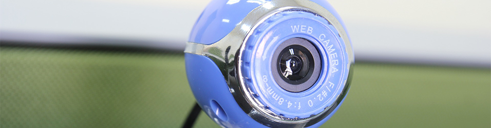 This is an image of a circular light blue Webcam in the middle of the image. The backdrop is green and white and neutral.